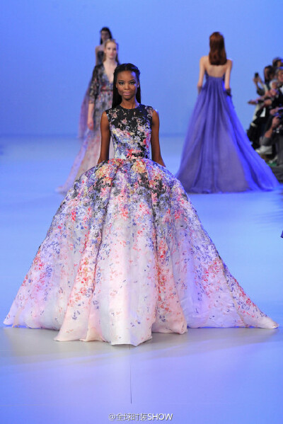 Elie Saab（艾丽·萨博）2014春夏系列高级定制时装，Elie Saab将五颜六色的花朵汇聚到了以渐变色为底色的裙装上，加上模特走动时摆动的裙摆效果，让整套礼服恰似正在生动地上演着一场从天空飘洒下的花雨。
