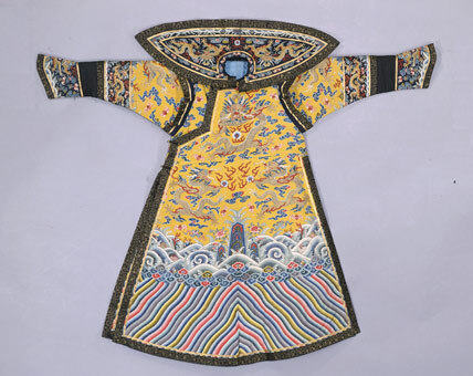 明黄缂丝彩云金龙纹女绵朝袍·前式。清嘉庆，身长139cm，两袖通长174cm，袖口21cm，下摆118cm，开裾长81cm。清宫旧藏。 朝袍圆领，大襟右衽，马蹄袖，袖、身相接处有接袖，有披领、护肩，左右开裾。袍以“通经断纬”的缂丝法周身织金龙5条，间饰五彩云蝠纹，并用彩色纬线以晕色法织海水江崖纹，祥云、平水、立水分别用三色、四色、九色织成。衣缘镶石青色缠枝莲纹织金缎边，无背云。袍衬月白色暗花绫里，中絮薄绵。 此朝袍缂工以平缂为主，有多处动笔晕染，但仍不失为一件缂丝精品，为清嘉庆皇后冬季所穿。朝袍原有布条，上书：“西暖殿”。