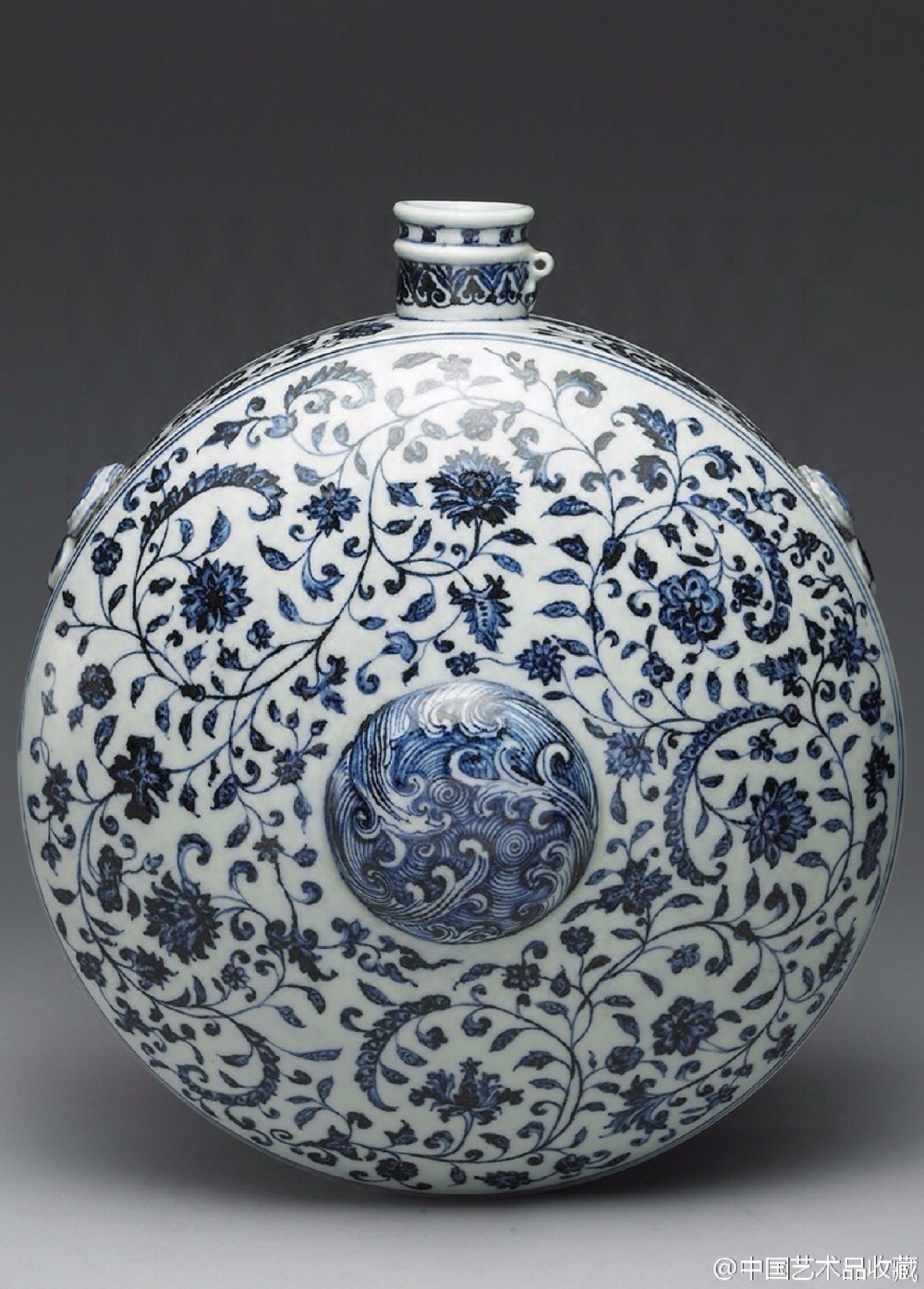 【 明永乐 《青花花卉纹扁壶》】高38.8cm，口径5.4cm，背径34.4cm；带座高45.5cm，宽36.5cm。台北故宫藏。器形仿自西域水囊造型，附镂雕双龙抢珠红木座。壶整体呈扁圆形，小圆唇口，口旁有一圆系，应是系壶盖之用，细颈，中部隆起弦纹一道；正面微凸，中心隆起，背面平整无釉，中心为圆形凹入。