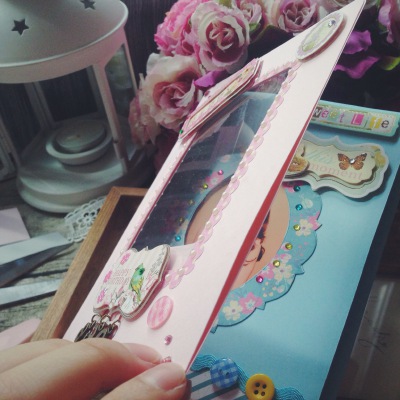 缤纷剪贴手作：定制生日手工贺卡，迷你相册。镂空相框样式封面，珍珠围绕的波点花边框，金属日期数字挂件，立体复古贴纸。透过封面透明板，可以看到里蓝色小碎花边框的相框，框上篮、黄、粉渐变闪钻围绕，增加层次感…